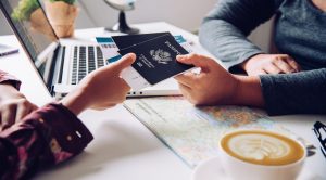 Two people sit at a table with a laptop, map, and coffee; one hands passports and boarding passes to the other, possibly discussing travel plans or seeking advice from a Grand Prairie K-1 fiancé visa attorney.