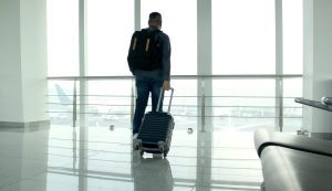 A man with a backpack and suitcase stands in an airport terminal, looking out the window at airplanes on the tarmac—perhaps seeking guidance from a Fort Worth immigration attorney for his upcoming journey.