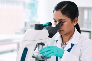 A scientist in gloves and a lab coat examines a sample through a microscope in a laboratory, similar to the careful analysis provided by an Arlington temporary protected status lawyer.