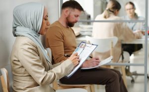 A woman in a hijab and a man sit in a waiting area filling out forms, while two people have a discussion at a table—an everyday scene for an Arlington temporary protected status lawyer’s office.