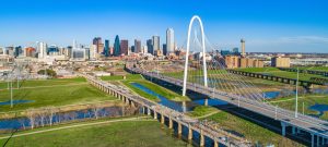 Aerial view of a modern cable-stayed bridge spanning a river with the Dallas city skyline in the background, near Grand Prairie K-1 fiancé visa attorneys, on a clear, sunny day.