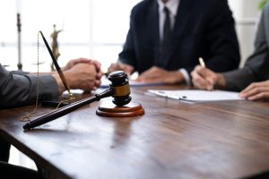 A gavel rests on a wooden table as three people in suits sit around it, two of them signing documents related to a Houston family based visa.