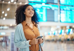 A woman holding a passport and ticket stands in an airport terminal, looking up at flight information screens—perhaps anticipating her Adjustment of Status Houston interview as she navigates her immigration journey.
